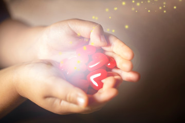 光を放つ沢山の赤いハートのモチーフを持つ子供の手