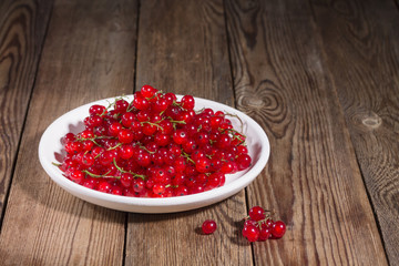 Fresh red currants in a white plate on a natural wooden table. Copy space. Healthy eathing.