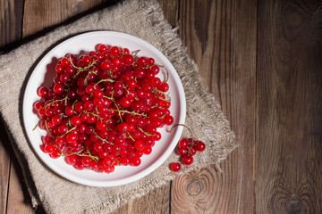 Fresh red currants in a white plate on a natural brown wooden background on linen napkin. Rustic style. Flat lay