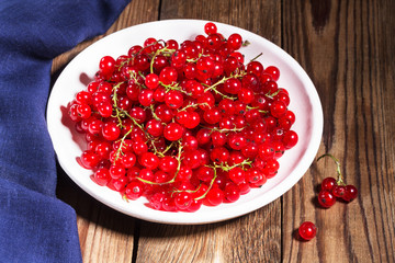 Fresh red currants in a white plate on a natural brown wooden table on line blue napkin. Rustic