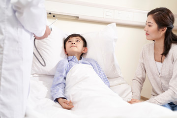 Obraz na płótnie Canvas five year old asian kid lying in bed in hospital ward accompanied by mother