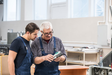 Senior and young printing workers in overalls standing in workshop and using scanning device for examination