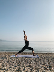 Fototapeta na wymiar Young blond girl practice warrior yoga asana on sea shore at sunrise