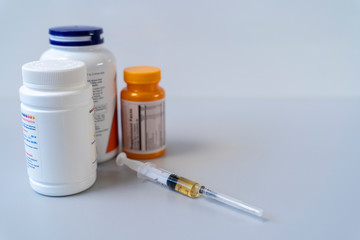 A disposable injection syringe lies on a table next to plastic jars.