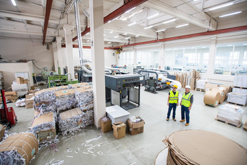 Workers of paper recycling factory wearing reflective vests standing in shop with packaged papers...