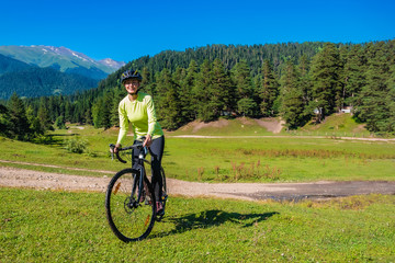 Obraz premium A young smiling girl on a cyclocross bike rides a green bright meadow against the background of a coniferous forest and a rural road