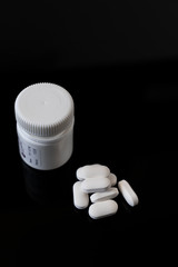 White pills and jar on a black background.