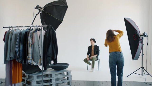 Backstage of professional photo shoot in studio: handsome young man is posing for camera and woman is taking pictures with modern digital camera.