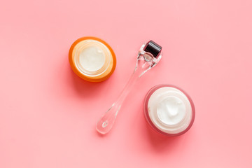 Dermaroller for mesotherapy near creams on pink background top-down flat lay