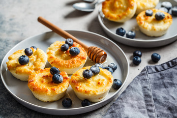 Cottage cheese pancakes with blueberries and honey, gray background. Russian cuisine concept.