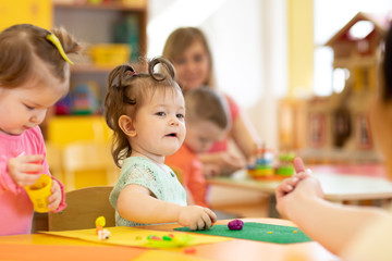 Nursery children with teacher play colorful clay toy in daycare or kindergarten
