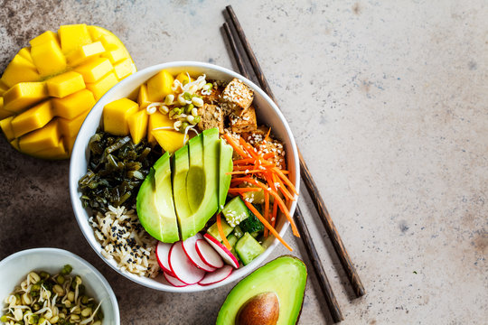 Vegan poke bowl with avocado, tofu, rice, seaweed, carrots and mango, top view. Vegan food concept.