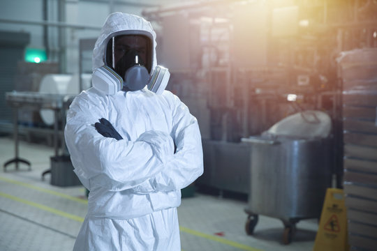 man in chemical protection clothes and toned mask in a factory against the background of an industrial workshop looking into the frame. 