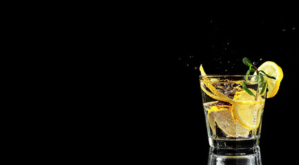 Cold drink on a black background. Spray from falling ice in a drink. One glass with lemonade or mojito, a cocktail with lemon and mint. Copy space, close up.