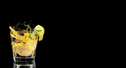 One glass with lemonade or mojito, a cocktail with lemon and mint. Cold drink on a black background. Spray from falling ice in a drink. Copy space, close up.