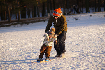 Young man learning his small child how to ski. Sunny photo on background of winter snowy park