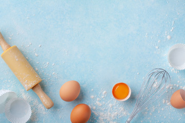 Baking background with rolling pin, whisk, eggs, flour on blue table top view. Flat lay.