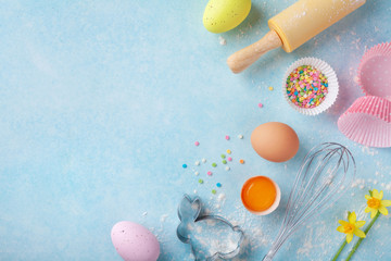 Easter baking background with rolling pin, whisk, eggs, flour and colorful confetti on blue table...