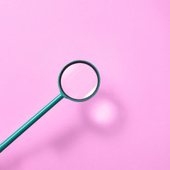 Magnifying glass above pink background with shadows.