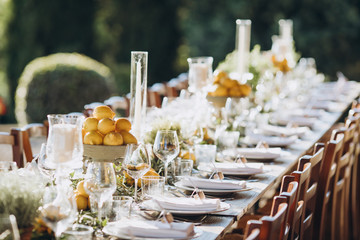 in the back yard of the old villa there is a long festive table, which is decorated with lemons and herbs, on the table are plates, glasses and candles. Wedding in Italy. Tuscany