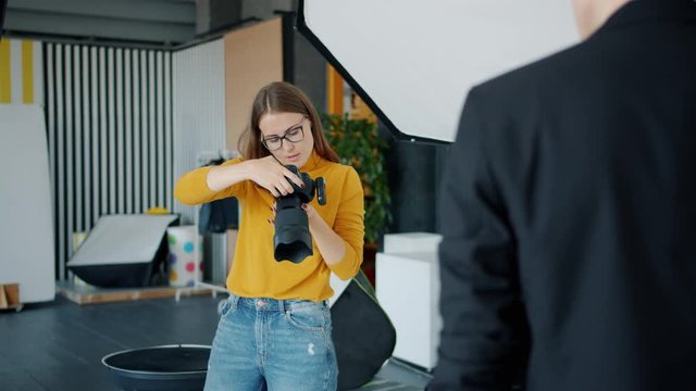 Professional photographer attractive young lady is taking pictures of male model using camera in modern studio enjoying work with a handsome man.