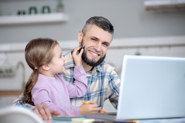 Dad with daughter in her arms sitting in front of laptop.