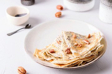 Crepes with poppy seed served with honey and pecans on grey background. Pancake week, mardi gras, maslenitsa holidays. Selective focus