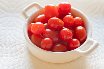 Cherry tomatoes in a small glass bowl close up on white background