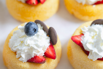 Biscuit cakes with fresh strawberries, blueberries, chocolate, and whipped heavy cream. Fresh mini biscuit cups close up on white background.