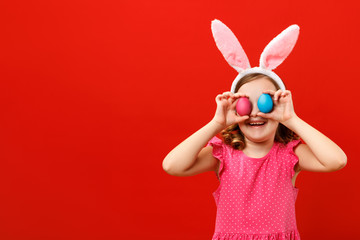 Happy cheerful little girl holding two easter eggs. Close up portrait of a child on a red background. Copy space