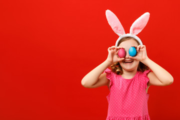 Happy cheerful little girl holding two easter eggs. Close up portrait of a child on a red...