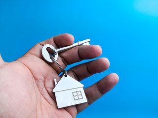 Hand holding key with home keychain over blue background