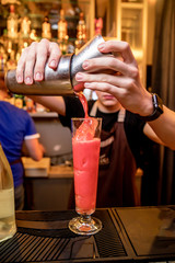 A bartender in a nightclub pours a cocktail from a shaker into a glass glass with ice