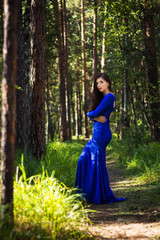 Obraz na płótnie Canvas Beautiful, young girl dressed in a blue dress, on a background of a pine forest.