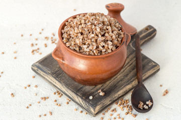A small clay pot with buckwheat porridge on a wooden board on a light background with copy space. Selective focus.