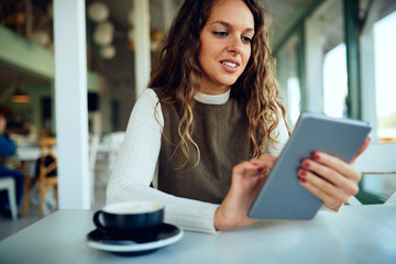 Attractive young curly brunette looking at her tablet and smiling	