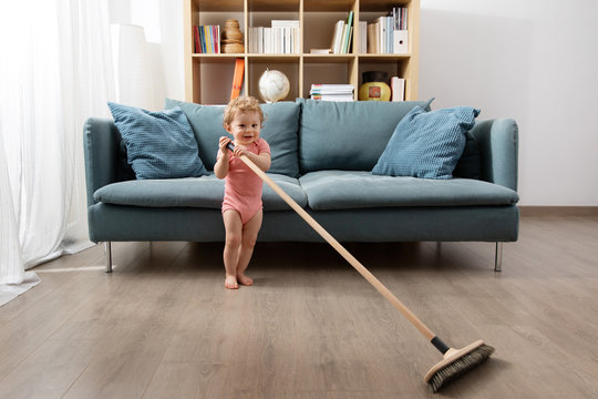 Cute toddler sweeping living room floor with broom