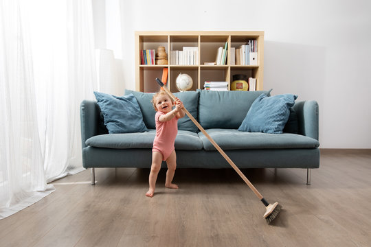 Happy baby sweeping living room floor with broom