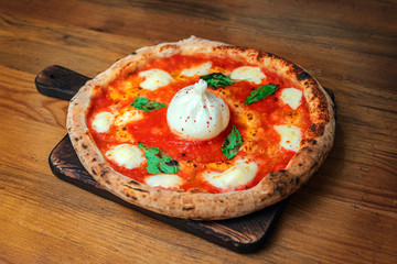Freshly baked pizza with cheese, sauce, tomato, basil and burrata on a wooden table