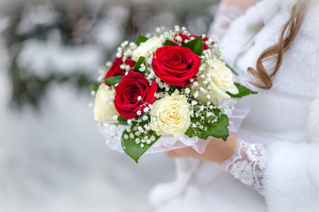 The bride holds a bouquet of red roses against a background of snow-covered trees