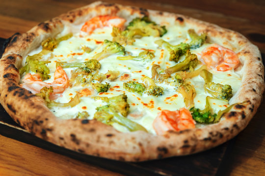 Freshly baked pizza with cheese, sauce, shrimps and broccoli on a wooden table close up