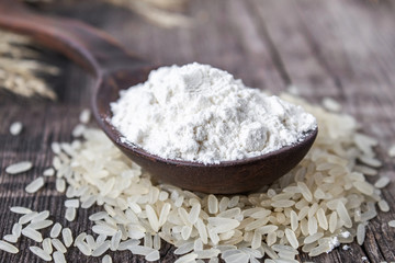 Rice flour in a spoon on a pile of white rice on old boards.
