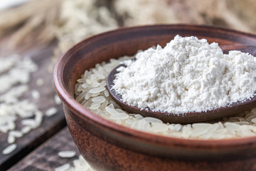 White rice in a bowl with a spoon of white flour on a background of old boards. Jasmine rice for cooking.