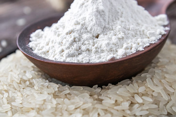 Rice flour in a spoon on a pile of white rice on old boards.