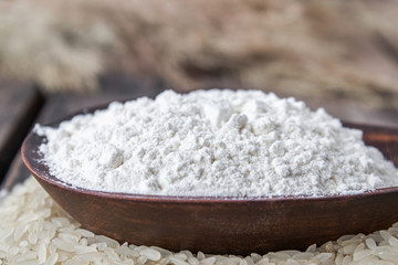 Rice flour in a bowl on a pile of white rice on old boards.