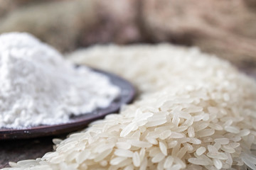 Rice flour in a bowl near the heap of white rice on old boards. Jasmine rice for cooking.