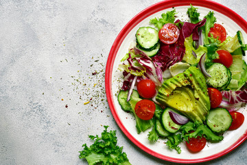 Fresh vegetable salad with avocado, tomatoes, cucumber and red onion. Top view with copy space.