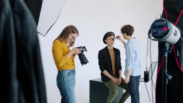 Slow motion of make-up artist working with male model in photo studio while photographer is using camera before photoshoot. People and occupation concept.