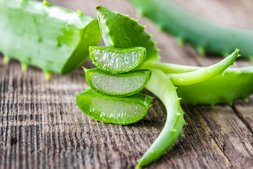 Fresh aloe vera leaves and slices of aloe vera on a wooden background.
