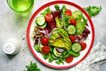 Fresh vegetable salad with avocado, tomatoes, cucumber and red onion. Top view with copy space.